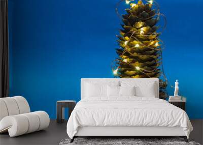 A spruce cone on a blue background is decorated with a lights garland as decoration for Christmas and New Year. Wall mural