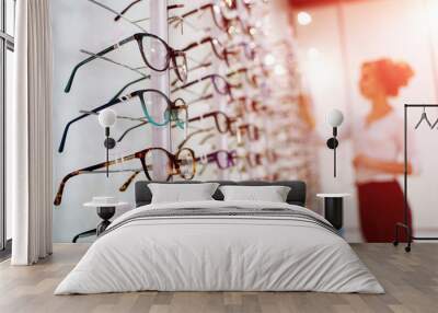 eyeglasses shop. stand with glasses in the store of optics. woman on blurred background chooses glas Wall mural