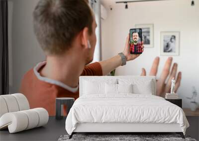 A male friends are talking online via video while staying at home. A guys is using smartphone for video call, zoom Wall mural