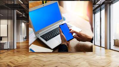 A man is chatting on the phone while working with laptop in office. Closeup. Copy space on a blank laptop screen, empty phone screen Wall mural