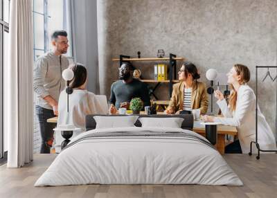 A team of young and successful employees listen to progress report from female employee at a morning meeting. Multiracial team in the office Wall mural