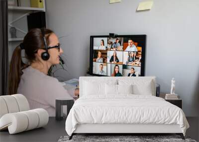 A young female superior is listening to reports of her subordinates using a video app on PC, a back shot, hand are on the desk. Wall mural