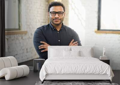 Ambitious hindu man in smart casual shirt stands with arms crossed in contemporary office space and looks at camera, portrait of purposeful indian businessman, ceo indoor. Diversity of office staff Wall mural