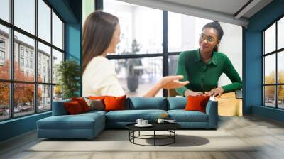 Confident businesswoman, executive manager, ceo talking to African-American female coworker, discussing strategy. Diverse female partners brainstorming in meeting room, multiracial woman takes notes Wall mural