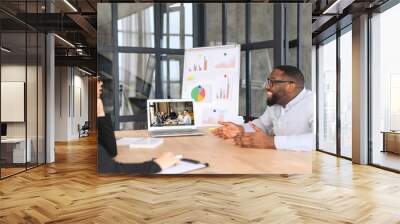 Diverse work team has virtual meeting with outsource team, multiracial colleagues sit at the desk in modern office space and talking via video call with group on the laptop screen, video conference Wall mural