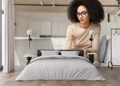 Elegant young adult female psychologist, working at home, writing down in her diary, sitting at the laptop, consulting the client online, talking, feeling confidently, love her work, support others Wall mural