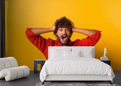 Excited shocked man holding hands on face and screaming looking at camera with big eyes and open mouth, shocked bemused with news, win at lottery. Indoor studio shot isolated on orange background Wall mural