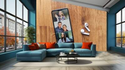 Flat lay of a phone lays on the wooden table, a few of people profiles on the screen, airpods headphones near. App for video communication on phone screen, zoom on smartphone Wall mural