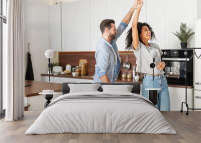 Handsome white man and attractive African American young woman is cooking and having fun together while cooking on the kitchen, romantic interracial couple is dancing while preparing lunch or dinner Wall mural