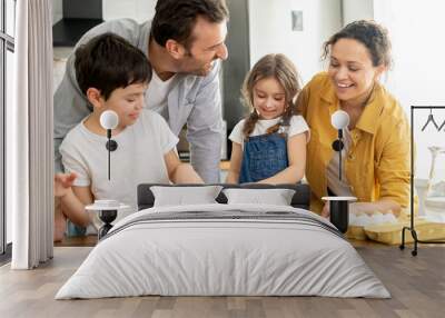 Happy family of four cooking in the kitchen together, parents and two kids making dough together, preparing pie or cookie, have a fun on weekend Wall mural