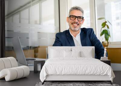 Happy smiling middle aged professional business man company executive ceo manager wearing blue suit sitting at desk in office working on laptop computer laughing at workplace. Portrait. Wall mural