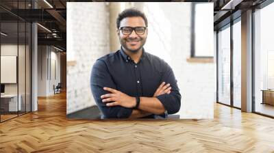 Headshot of skilled hindu male employee standing with arms crossed in modern office, successful confident mixed-race man wearing eyeglasses and smart casual, business portrait of indian entrepreneur Wall mural