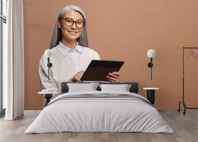 Modern elderly senior woman in formal wear using digital tablet isolated on beige. Portrait of mature female office employee using online technology for doing business, computer app for accounting Wall mural