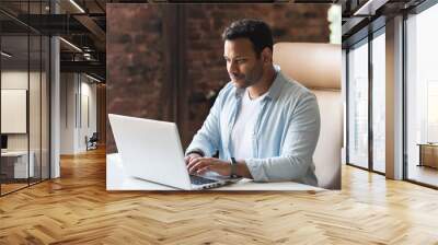 ndian developer guy is working with a laptop sitting at the desk indoors. A young multiracial guy in smart casual wear is typing on the keyboard, answering email, communicates with the customer Wall mural