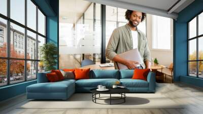 Portrait of confident African-American businessman standing with laptop, male office employee in smart casual wear looking at the camera and smiles, leaned back at te desk, ceo, manager, sturtup owner Wall mural