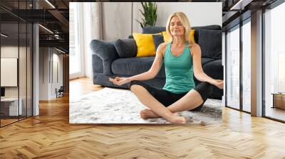 Relaxing antistress yoga at home. Mature woman in a easy pose sits on the floor in sportswear barefoot. Training at home concept Wall mural