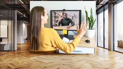 Remote work. A young woman has video meeting with an african-american coworker, employee. She waving hello into webcam. Back view Wall mural