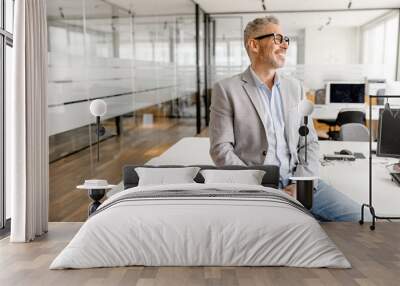 Serene modern middle aged businessman in formal wear leaned on the desk looking away, inspired and calm mature business owner at the office, confident grey-haired man in relaxed pose Wall mural