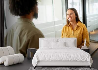 Two colleagues have pleasant conversation standing in the walkhall of the modern open space office, smiling and enjoying friendly working atmosphere, smiling woman listening her male coworker Wall mural