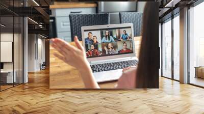 Video call, zoom. Icons of a group of people on laptop screen, app for video online communication. A woman is waving hello in webcam, back view Wall mural