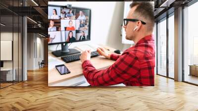 Video conference call of a young man in office. A side back view of a young man talking via web camera to bunch of people at the workplace, he hold a pen in his hand Wall mural