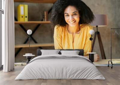 Video screen of beautiful mixed-race girl with an afro hairstyle. The woman in smart casual wear sits i n the office and looks at camera with a frienly smile Wall mural