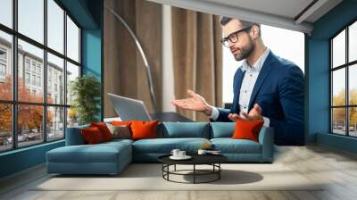 Worried disturbed young bearded businessman office manager sitting at the desk and video calling, having an emotional conversation with family, or client online on a virtual call via laptop, gesturing Wall mural