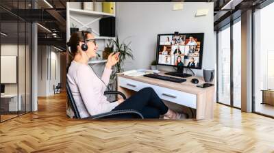 Young successful employee is have a meeting with her team using a headset, she is sitting relaxed and smiling, a middle side shot. Wall mural