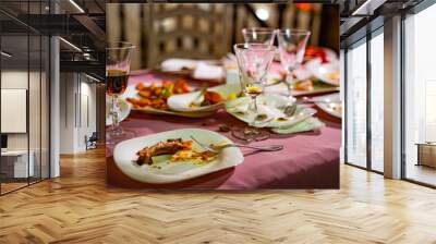 Plates with crumbs of food and glasses for wine on the table with pink tablecloth in the restaurant. Remains of food in plates after lunch or dinner. Wall mural