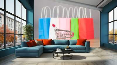 Small metal cart and colorful paper shopping bags on wood table background. Wall mural