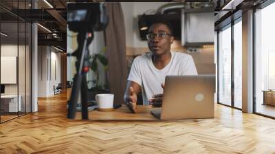 Happy young smart black blogger man filming new vlog video with professional camera in kitchen at home slow motion. Wall mural