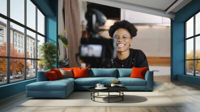 Happy young successful female black vlogger making new video for blog using professional camera at home slow motion. Wall mural