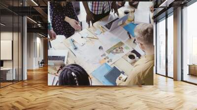 Top view of young team working on architectural project. Group of mixed race people standing near table and discussing. Wall mural