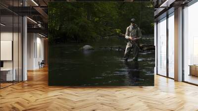 Fisherman catching brown trout on spinning tackle standing in river. Wall mural