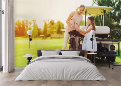 A girl and a woman get the golf clubs out of the bag Wall mural