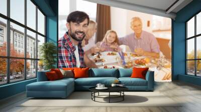 A man is smiling and posing sitting at a festive table on Thanksgiving Day. Against the background of his family Wall mural