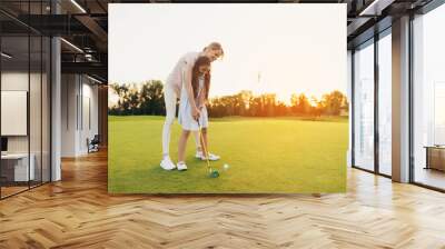 a woman is teaching a girl to play golf. the girl is preparing to hit, the woman is standing behind  Wall mural