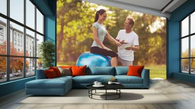 Man and woman doing yoga exercises in the park. A man is training a woman Wall mural