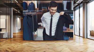 Successful young businessman measures jacket in business mens clothing store. Wall mural