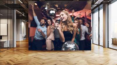 Young people have fun in a nightclub and sing in karaoke. In the foreground there is a woman in a black dress. Wall mural