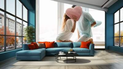 Couple girl and guy play with pillows near window. Wall mural