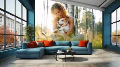 young red-haired woman sitting on green grass in the park holding jack russell dog in her arms. Wall mural