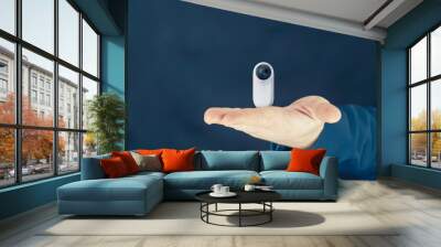 A man holds a compact white 360-degree Action Camera in his hand. Wall mural