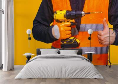 Male worker holds a close-up electric cordless screwdriver in his hands against a orange background Wall mural