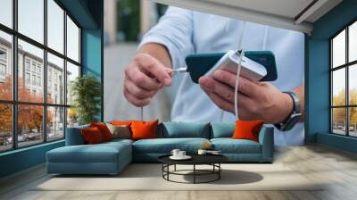 Man charges a smartphone with a power bank in hand. Portable charger for charging gadgets. Wall mural