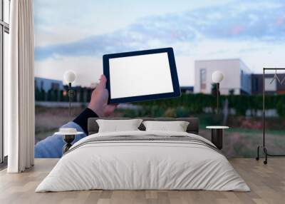 Mock up of a tablet with white screen in hand, against the background of modern houses. Wall mural