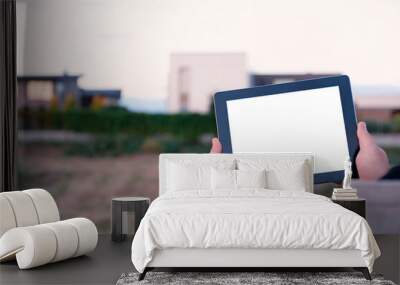 Mock up of a tablet with white screen in hands, against the background of modern houses. Wall mural