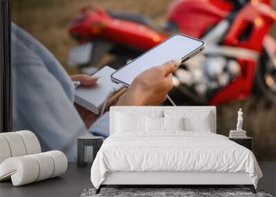 The girl holds a smartphone in her hands. Power Bank charges the phone against the backdrop of a motorcycle and nature. Wall mural