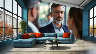 A businessman in a suit engaging in conversation with two women. They are likely discussing business matters or having a professional meeting in a formal setting. Wall mural