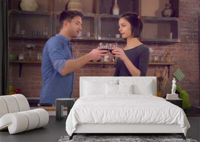 Happy couple cooking dinner on the kitchen. Young people cook salad drinking wine toasting enjoy evening talking. Beautiful couple in love on a romantic date at home. Wall mural